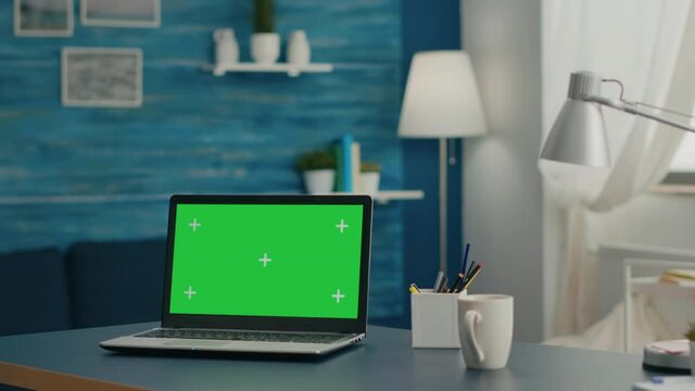 Laptop computer with mock up green screen chroma key display standing on table in living room. PC with isolated display in home office studio with nobody in it