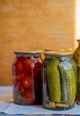 Glass jars with pickled cucumbers (pickles), pickled tomatoes and cabbage. Jars of various pickled vegetables. Canned food in a rustic composition.