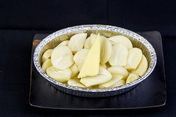 Peeled garlic, sliced ​​in a cup foil on a tile tray.
