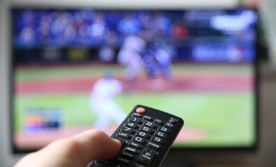 Baseball im Fernsehen schauen. Finger auf die Lauter-Taste auf der Fernbedienung. (Fokus auf der...
