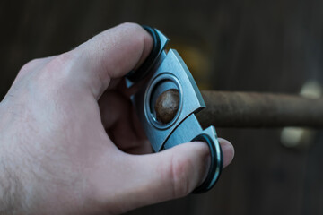 A man's hand trims the edge of a cigar with a guillotine