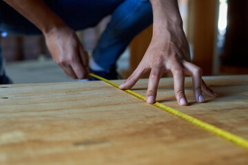 Young carpenter with a beard and white t-shirt with a measuring device measuring the distance of the wood in a house under construction man with hard hats on his head working on a wood work.