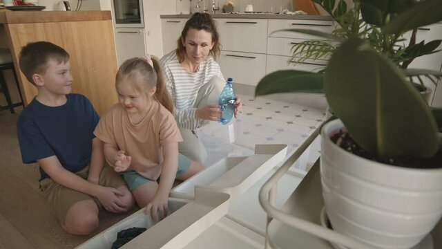 Lockdown of Caucasian boy and his little sister with down syndrome sitting on kitchen floor and helping their mommy segregating rubbish