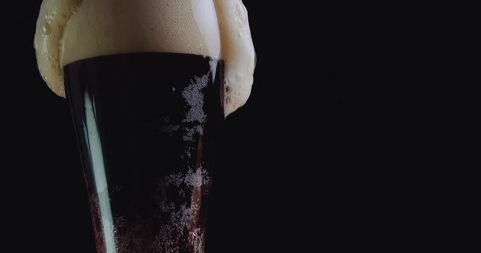 A glass beaker is filled with a brown carbonated liquid with the formation of foam that flows down its outer walls.