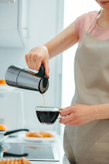 Young lady wearing apron making coffee at home