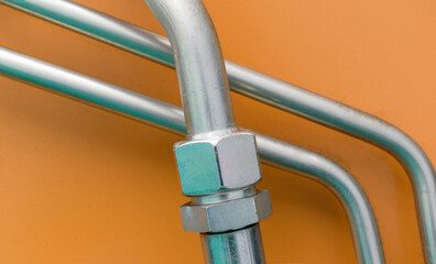 Obraz premium High pressure metal tubes. Union nut. White chrome plated metal with stainless properties. Orange background. Technological tubes concept.