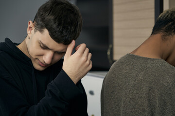 Staged photo illustrates problems and conflicts in gay couple relationships. Young upset and brooding man is standing behind his partner's back. 