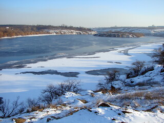 Panorama from the top of the hill of the frozen Dnieper covered with strong ice and dressed in a snow blanket on a frosty sunny day at sunset.