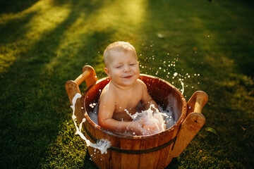baby splashes in a basin in nature on a green tvava, at sunset. Good mood, child's smile, happiness from swimming in water, water splashes fly, good summer day