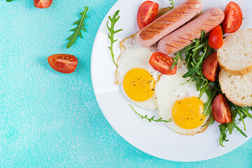English breakfast - fried eggs, sausages, tomatoes and fresh arugula. American food. Top view, flat lay