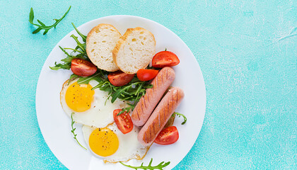 English breakfast - fried eggs, sausages, tomatoes and fresh arugula. American food. Top view, flat lay