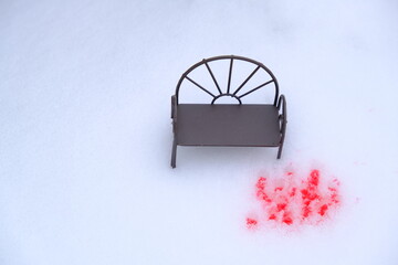 Miniature bench and red splatter on the snow. Selective focus.