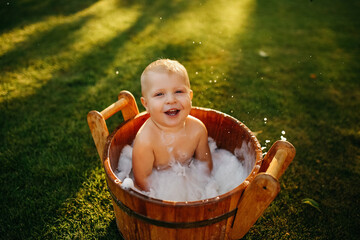 baby splashes in a basin in nature on a green tvava, at sunset. Good mood, child's smile, happiness from swimming in water, water splashes fly, good summer day