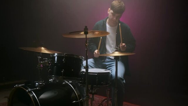 Drummer playing the drum set in a dark room on a black background.