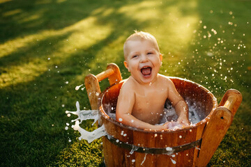 baby splashes in a basin in nature on a green tvava, at sunset. Good mood, child's smile, happiness from swimming in water, water splashes fly, good summer day