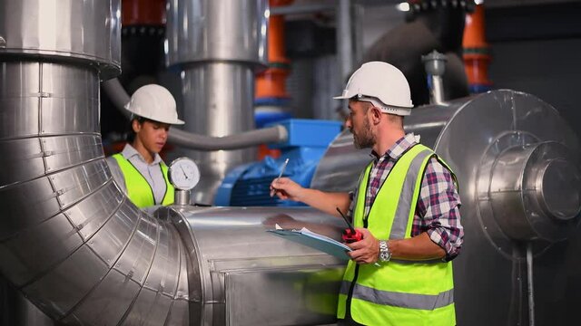 Industry engineer worker wearing safety uniform under checking the industry cooling tower air conditioner is water cooling tower air chiller HVAC of large industrial building to control air system.