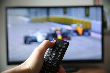 Watching formula 1 on TV. Thumb on the power off button on the remote (focus on the remote).