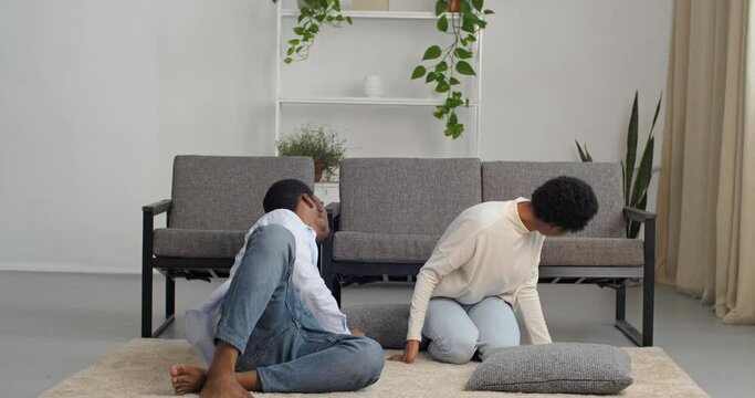 Couple young parents looking for child under sofa playing hide and seek with their daughter little girl hiding under sofa unexpectedly jumps out scares mom and dad, afro american family in living room