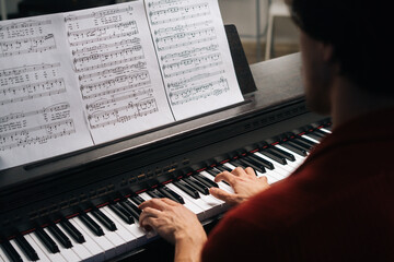 Top close-up view of hands of unrecognizable musician man playing on piano at home. Closeup back view fingers of pianist male playing digital electronic piano synthesize. Concept of music education.