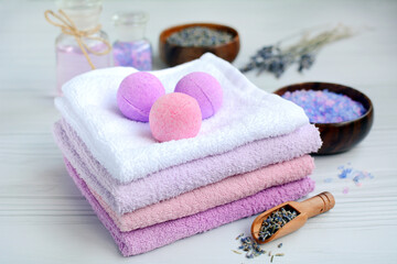 Close-up of a stack of colored towels with aroma balls and salt with lavender on a light wooden background. Concept of beauty treatments and spa