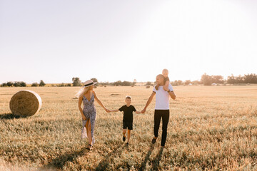 Fototapeta na wymiar happy family walks in the field near the haystack at sunset, mom dad and two sons, the family is happy with smiles on their faces, hug the children
