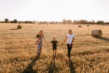happy family walks in the field near the haystack at sunset, mom dad and two sons, the family is happy with smiles on their faces, hug the children - Powered by Adobe