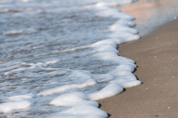Texture et volume de l'écume blanche d'une vague sur le sable fin d'une plage en pente, par un jour ensoleillé