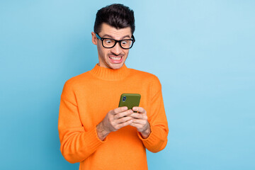 Photo of young man unhappy mad look smartphone dislike chat type sms isolated over blue color...