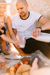 happy family had a picnic in the field near a haystack at sunset, mom dad and two sons drink milk eat croissants and fruits, the family is happy with smiles on their faces