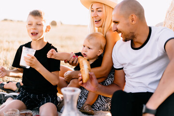happy family had a picnic in the field near a haystack at sunset, mom dad and two sons drink milk eat croissants and fruits, the family is happy with smiles on their faces
