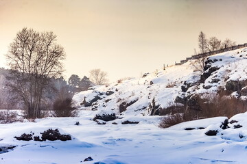 Winter landscape with frozen river, snow, rocks and trees
