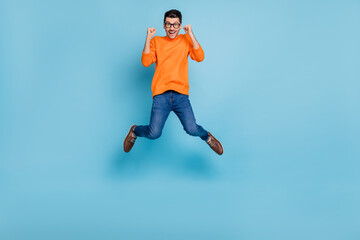 Fototapeta na wymiar Full body portrait of impressed handsome guy jump high fists up celebrate isolated on blue color background