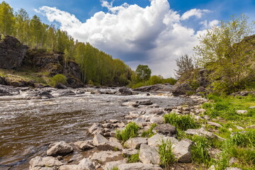 Fototapeta na wymiar Summer landscape with fast-flowing river, stone banks, trees and blue sky with white clouds