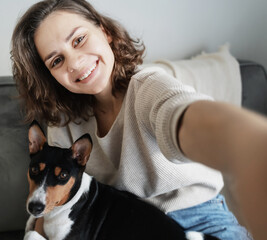 Pretty curly happy young woman smiling taking selfie on smartphone with dog