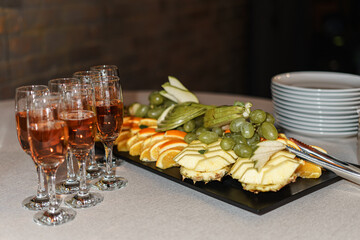 Glasses of champagne, fruits and plates stand on the table.