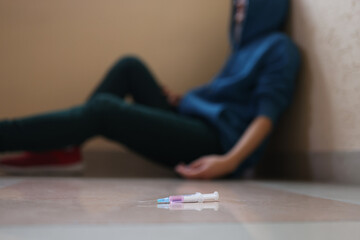 Addict sits in dark corner next to syringe with needle