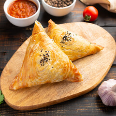 cutting board with delicious baked samosas on wooden background
