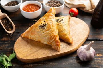 cutting board with delicious baked samosas on wooden background