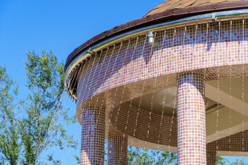 gazebo roof with water pipe and fountain in a city park, bright summer day