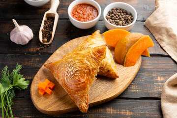 cutting board with delicious baked samosas on wooden background