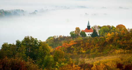 Naklejka premium a white church on a hill in an autumn landscape with a heavy fog background 