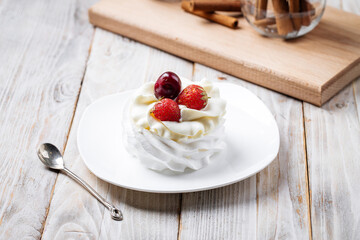 Pavlov dessert with whipped whites and berries on the wooden background