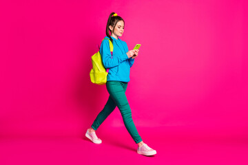 Fototapeta na wymiar Full length photo of adorable young lady wear blue sweater rucksack walking typing modern device isolated bright pink color background