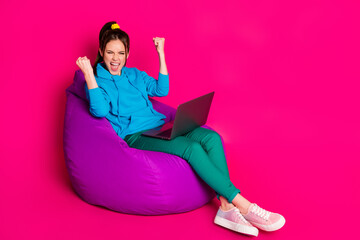 Full length photo of lucky lady wear blue sweater relaxing violet beanbag modern device rising fists isolated pink color background