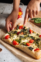 Slicing italian topping bread focaccia with spinach and tomatoes