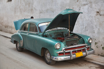 Havana. Cuba. A vintage car with its engine compartment open. The base of a person's head can be...