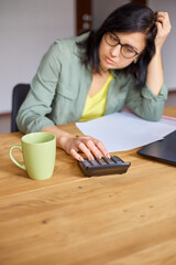 Woman accountant sit calculate expenses on calculator at wooden table, modern workplace