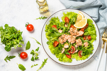 Green salad with baked fish at white table.