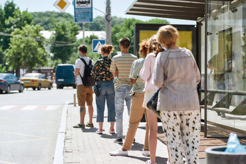 Full length shot of people wearing masks waiting, standing in line, keeping social distance at bus stop. Coronavirus, pandemic concept