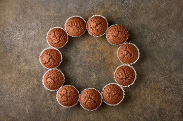 Chocolate homemade cupcakes laid out in the form of circle on wooden background, copy space, top view